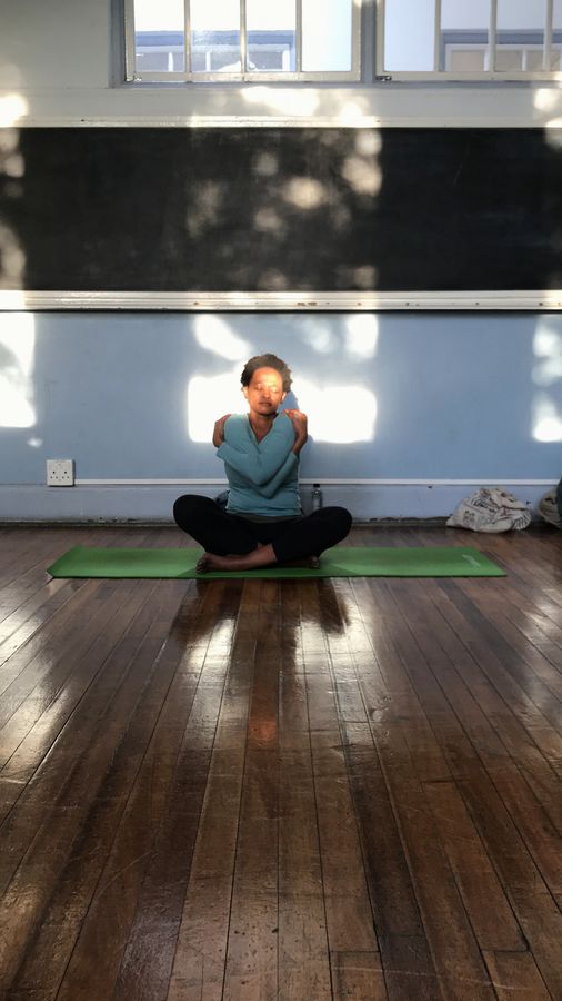 Sitting cross-legged on a mat in a light studio